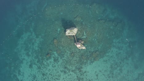 Aerial-View-Of-Small-Cottage-On-A-Rock-Formation-In-The-Middle-Of-Ocean-With-Clear-Blue-Water-In-Philippines