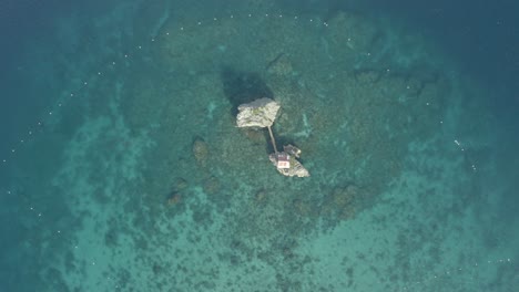 aerial view of small cottage on a rock formation in the middle of ocean with clear blue water in philippines