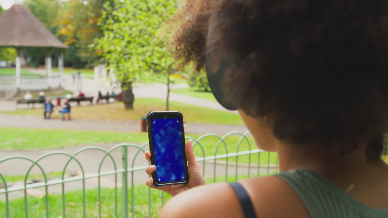 primer plano de una mujer al aire libre con auriculares inalámbricos transmitiendo programas o música desde un teléfono móvil