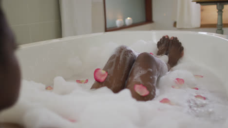 legs of african american attractive woman taking bath with foam and rose petals