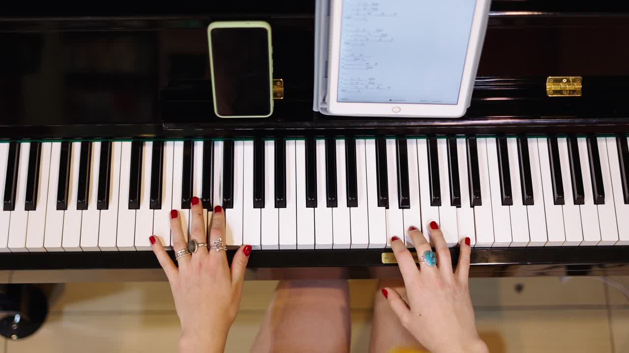 A person's hands playing a piano with a tablet displaying sheet music