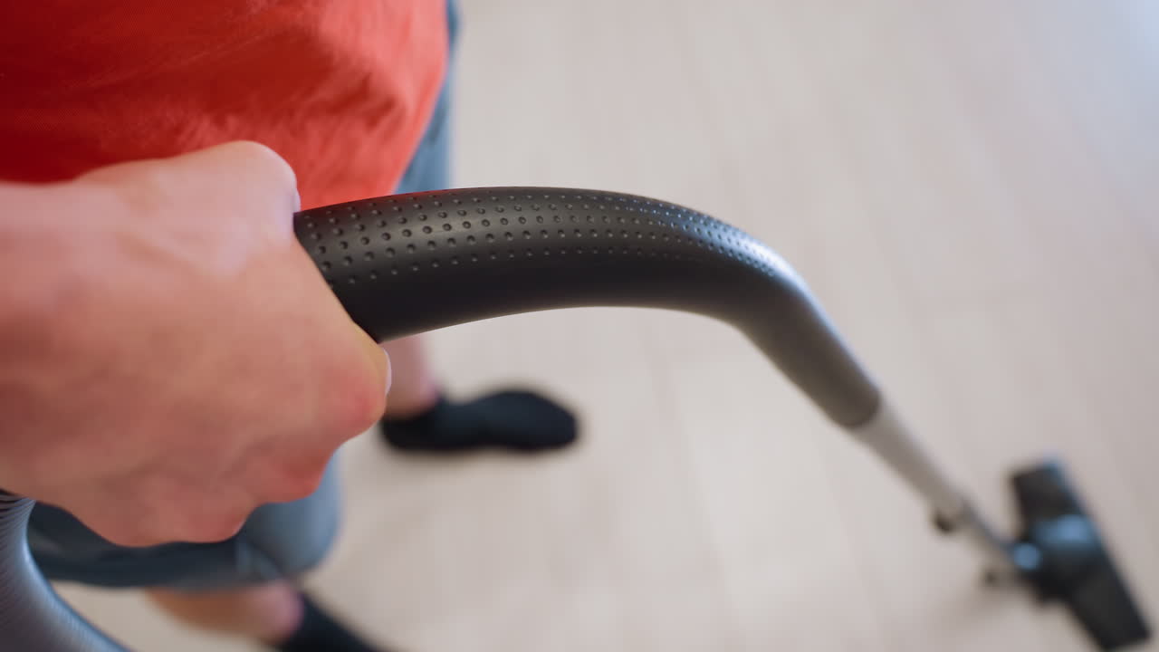 Close up of person gripping vacuum cleaner handle while cleaning light floor, showing detail of arm, hand, and cleaning action, representing daily household chores