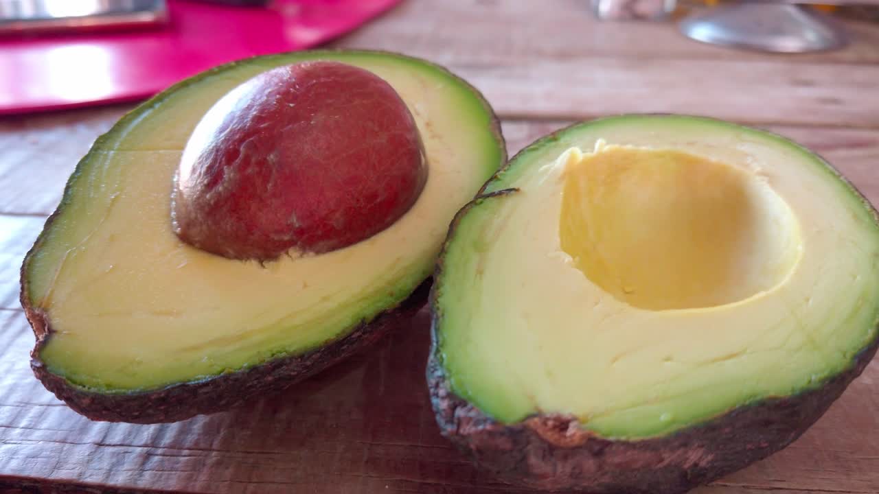 Close-up shot of a ripe avocado cut in half, revealing the seed and smooth yellow-green pulp on a rustic wooden table.