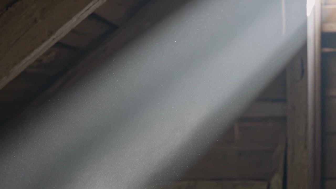 Schräg einfallender Sonnenstrahl dringt durch schmalen Lüftungsschlitz oben rechts im Loft ein, Staub tragend