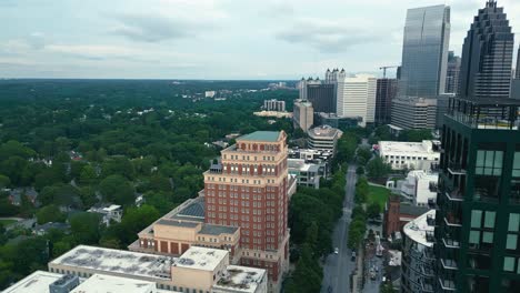 aerial flyover downtown of atlanta with skyscrapers and historic towers beside green forest trees. wide shot. cloudy day in summer. luxury high-rise buildings in usa.
