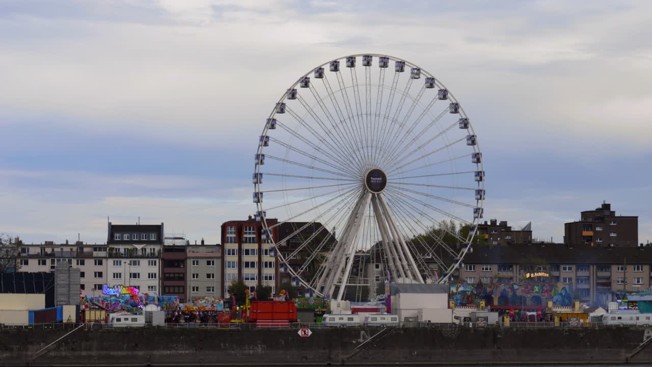 해질 무렵 라인강 옆에 있는 다른 놀이기구와 함께 쾰른의 축제에서 움직이는 대관람차의 슬로우 모션 공개