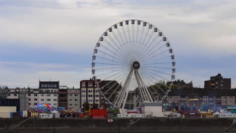 cámara lenta revela la toma de una rueda de la fortuna en movimiento en un festival en colonia con otras atracciones al lado del río rin durante el atardecer