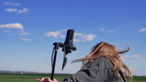 attractive girl with microphone on field. sexy young model with long hair in denim suit standing near the microphone and dancing looking at camera outdoors.