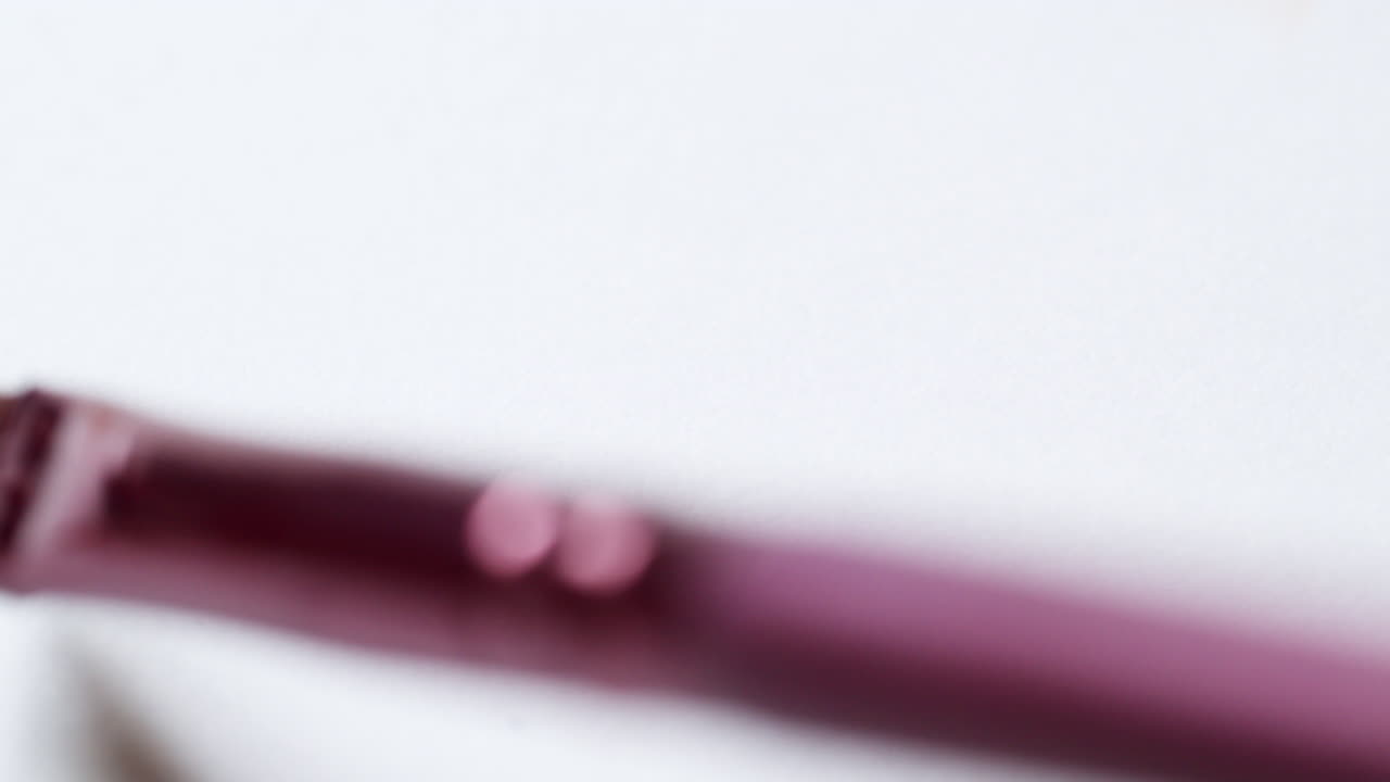 manchando un poco de bálsamo hidratante para los labios de color rosa melocotón, con un aplicador de pincel en una hoja blanca de papel