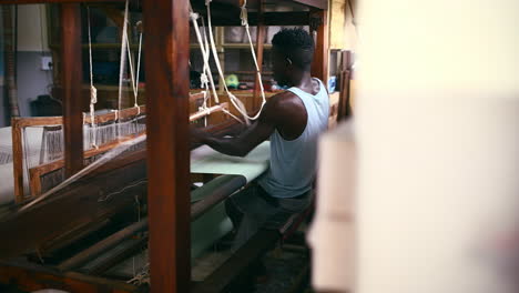 a young man operating a floor treadle loom inside