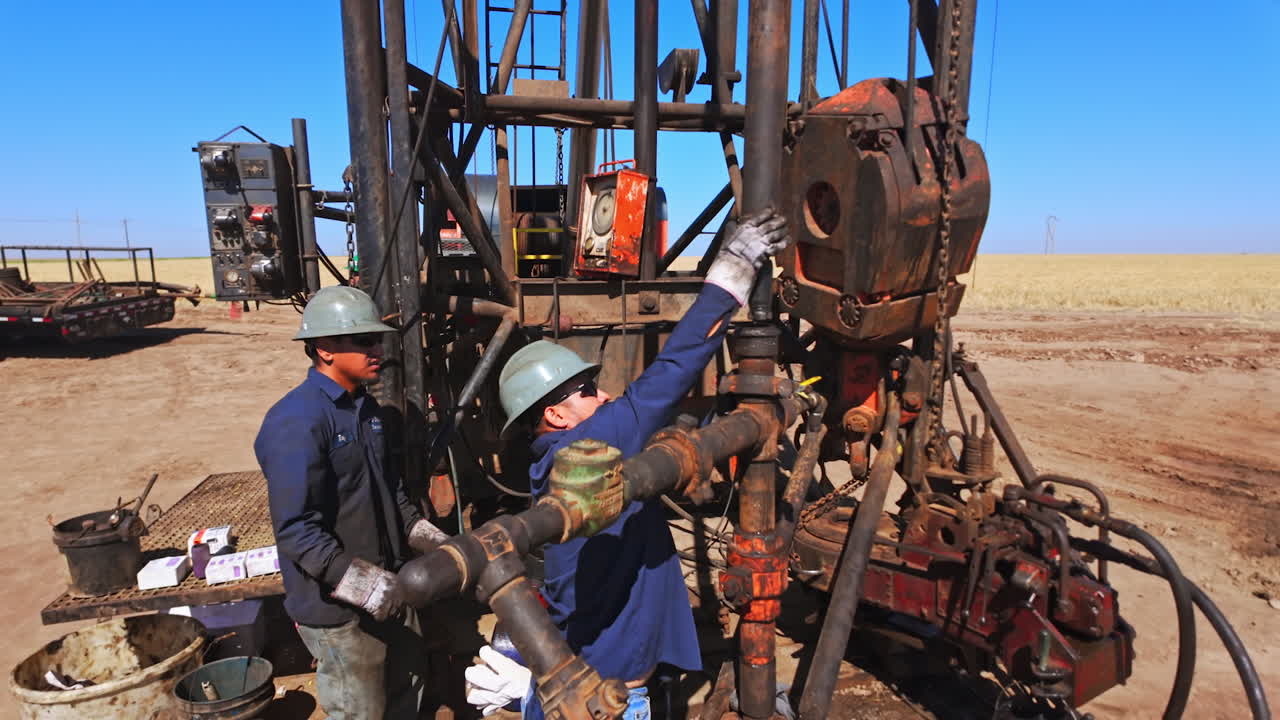 Workers connecting two pipes of drilling equipment. Men set the details of boring equipment in the field.
