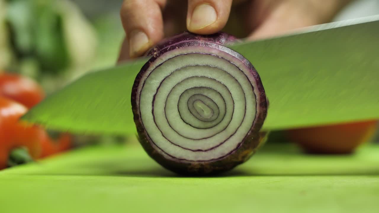 Slicing red onion on cutting board with Damascus steel knife, close up
