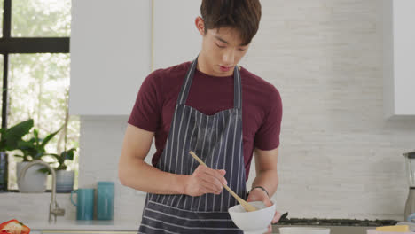 asian male teenager preparing food and wearing apron in kitchen