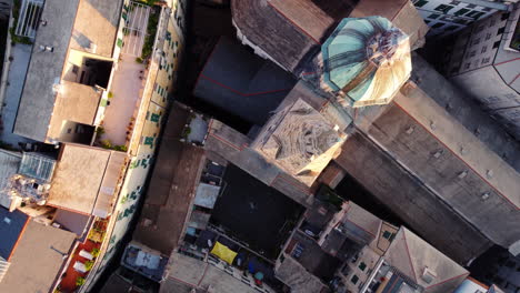 drone top-down shot over the historic center of genoa at sunset, showing rooftops, narrow streets, and a church structure with golden evening light