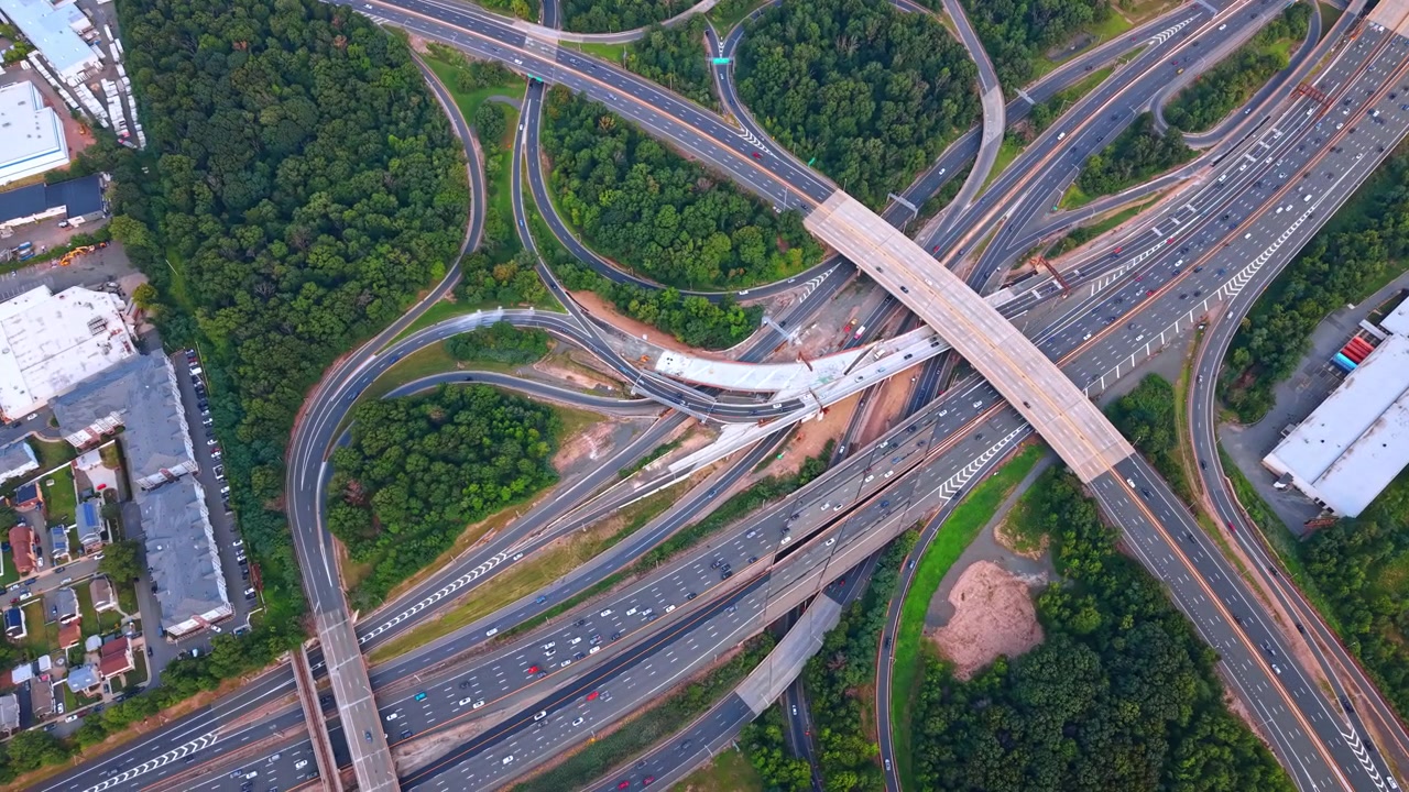 Highway junction with complex flyovers and ramps, New Jersey. Top down view of curving roads, vehicle traffic and surrounding green trees.