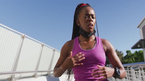 african american woman with lowered face mask using smartphone on the city bridge