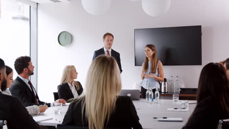 young businessman and businesswoman addressing group meeting around table at graduate recruitment assessment day