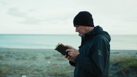 man walking near the sea in winter while reading a book