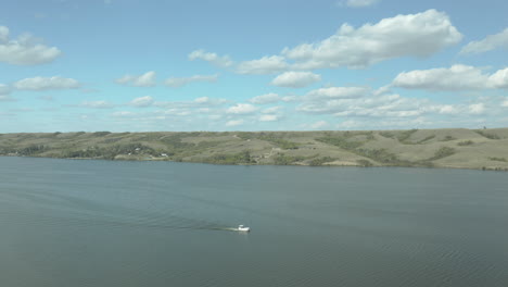 small boat sailing on huge lake, green hill in background