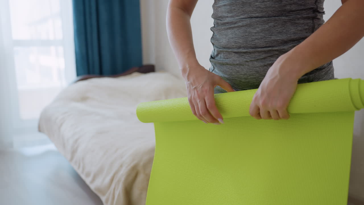 Close up of woman folding bright green yoga mat in cozy bedroom with natural daylight, casual fitness routine, calm preparation moment, active lifestyle indoors