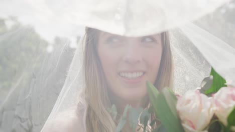 Portrait-of-happy-caucasian-woman-with-veil-on-sunny-day-at-wedding