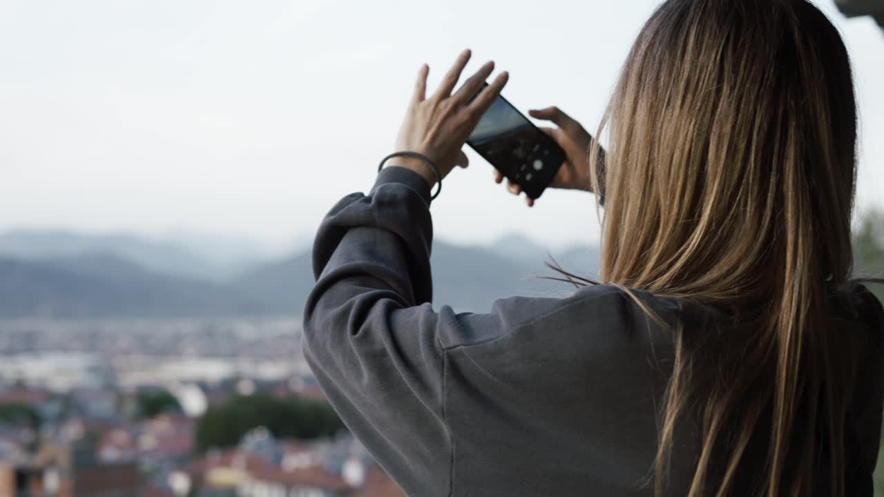 Donna scatta una foto, con un panorama sfocato di colline urbane sullo sfondo