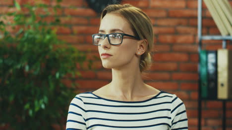 portrait of the beautiful young blonde woman in glasses and striped blouse turning her head to the camera and smiling nice