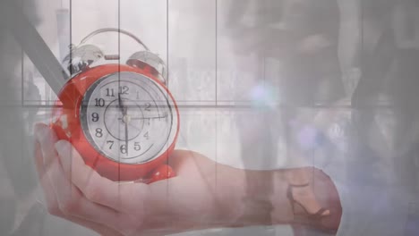 Animation-of-hand-holding-a-alarm-clock-against-time-lapse-of-businesspeople-walking-in-the-office