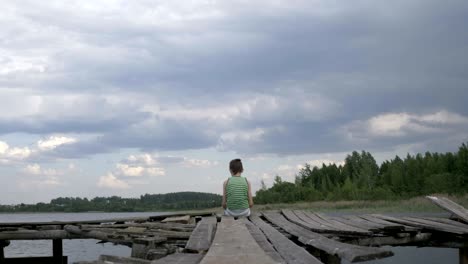 lonely boy sits on the edge of the pier in windy rainy weather, depression, thoughts about life