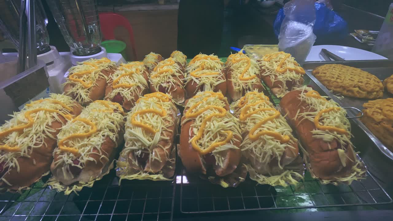 Multiple hotdog buns with grated cheese and sauce arranged on a display rack