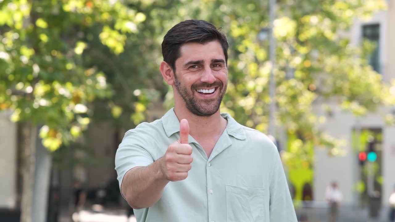 Happy man in casual shirt showing thumbs up at city park during sunny day