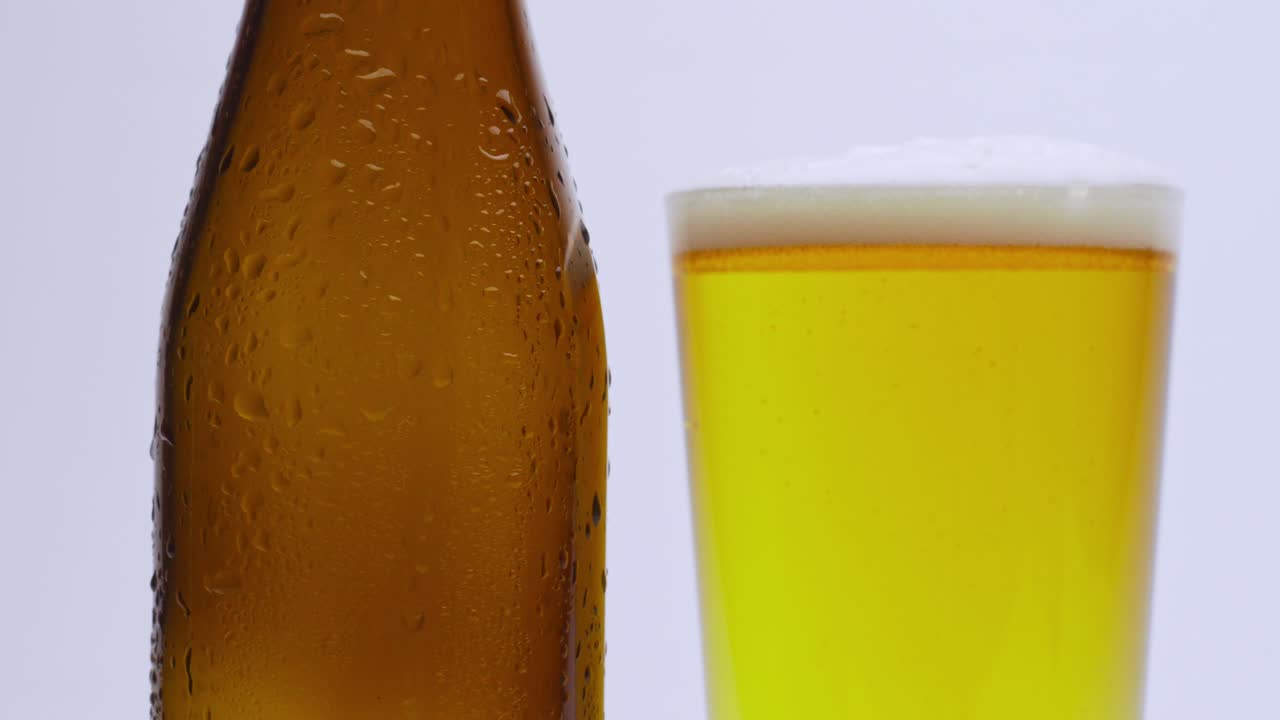 Ripresa al rallentatore di birra versata in un bicchiere, che mostra bollicine, schiuma e movimento dettagliato del liquido