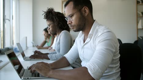 Thoughtful-man-in-eyeglasses-typing-on-laptop-at-office