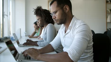 Thoughtful man in eyeglasses typing on laptop at office