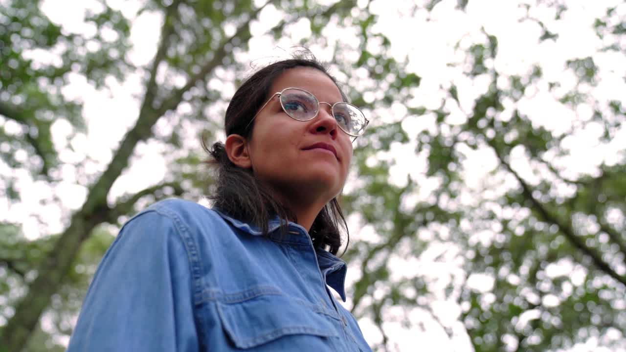 mujer étnica sonriente con gafas en el bosque