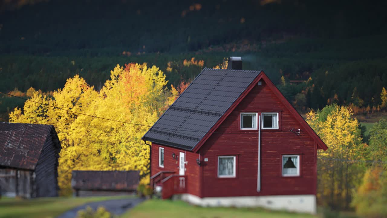 En lille rød træhytte står i efterårslandskabet ved foden af bjerget. Parallax-skud med bokeh-baggrund.