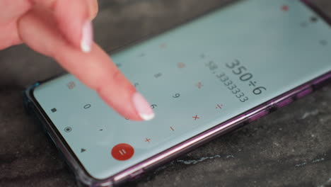 close up of lady with polished nails using calculator app on smartphone placed on dark table surface, finger tapping screen while performing calculation, focused on solving math problem