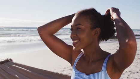 Nahaufnahme-Einer-Afroamerikanischen-Frau,-Die-Lächelt,-Während-Sie-Auf-Einer-Hängematte-Am-Strand-Sitzt