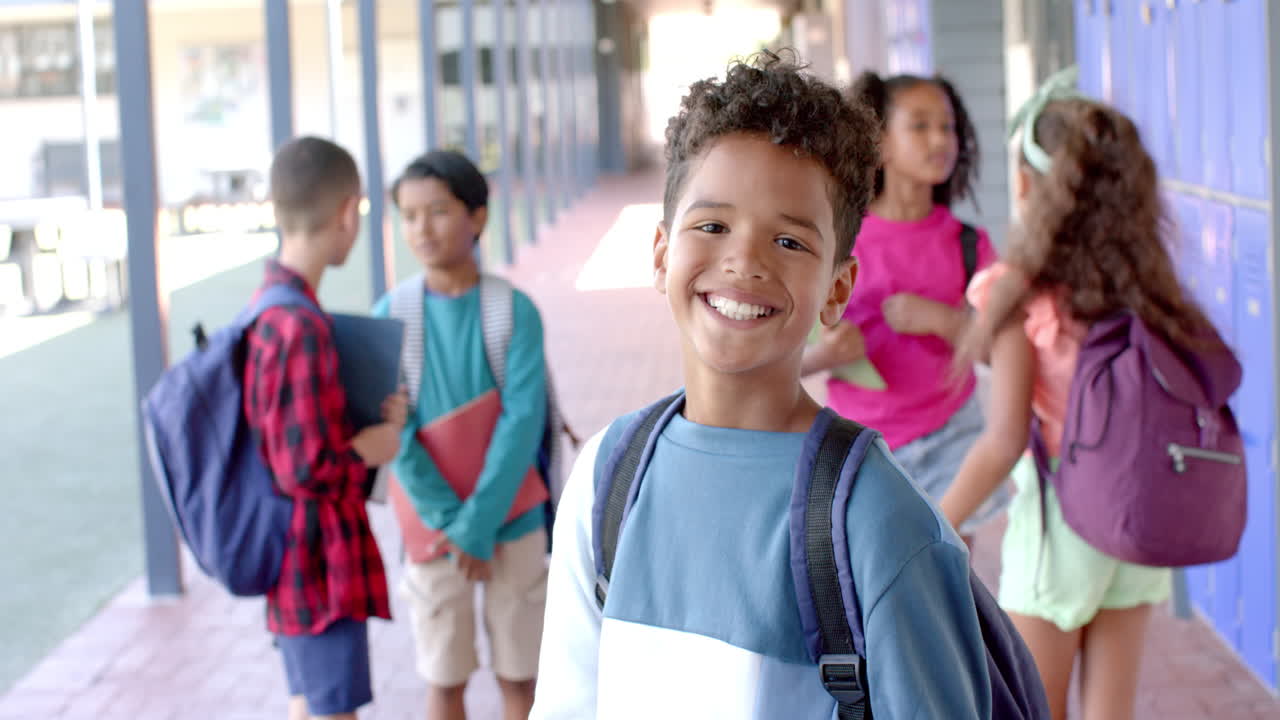 In a school corridor, a young African American student smiles at the camera