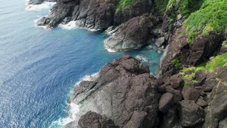 aerial orbit of incredible island landscape with jagged coastal boulders and turquoise ocean waves