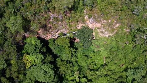 Descending-drone-aerial-wide-shot-of-the-cave-entrance-to-the-Enchanted-Well-or-Poço-Encantado-surrounded-by-trees,-plants,-and-cliffs-in-the-Chapada-Diamantina-National-Park-in-Northern-Brazil