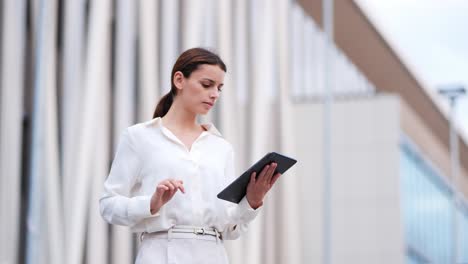 businesswoman walking walking past modern building while working on her tablet