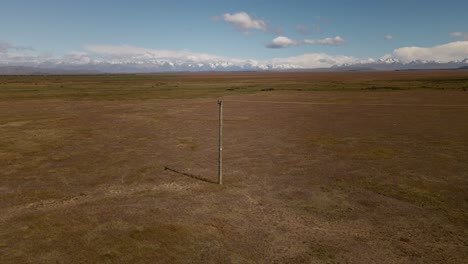 wooden power pole in the middle of endless dry plains with snow-capped mountains in background