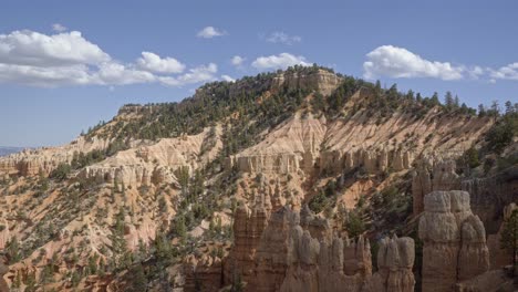 tilt up shot revealing a large orange sandstone mountain surrounded by hoodoo formations and pine trees in the desert of southern utah on a warm sunny summer day