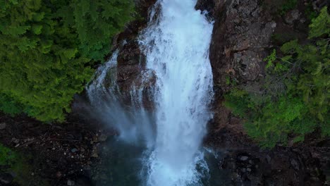 scenic fly over shot above flowing waterfall and evergreen forest in the pacific northwest