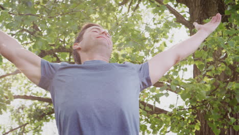 hombre al aire libre en ropa de fitness estirando los brazos y celebrando la naturaleza