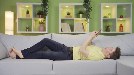 young man texting on the phone lying down at home.