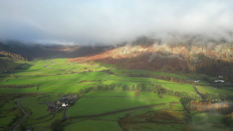 sunlit green valley surrounded by cloud shrouded mountains with camera pan revealing greater valley