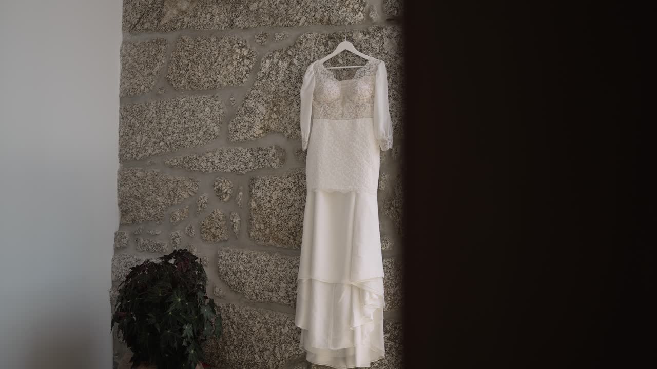 우아한  렌즈 웨딩 드레스가 질감있는 돌 벽에 매달려 시골적이고 만적인 분위기를 만니다.