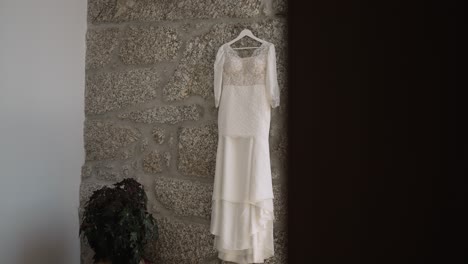 elegant white lace wedding dress hanging on a textured stone wall, creating a rustic and romantic atmosphere